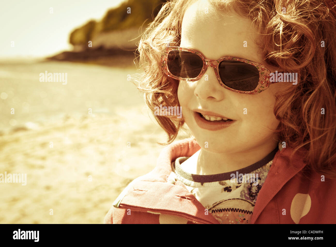 A five year old girl with red hair playing on the beach in Aberdovey, Wales. Stock Photo