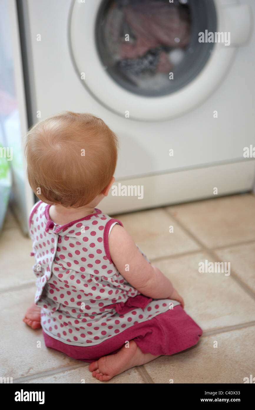8 month old baby girl looking at the washing machine Stock Photo