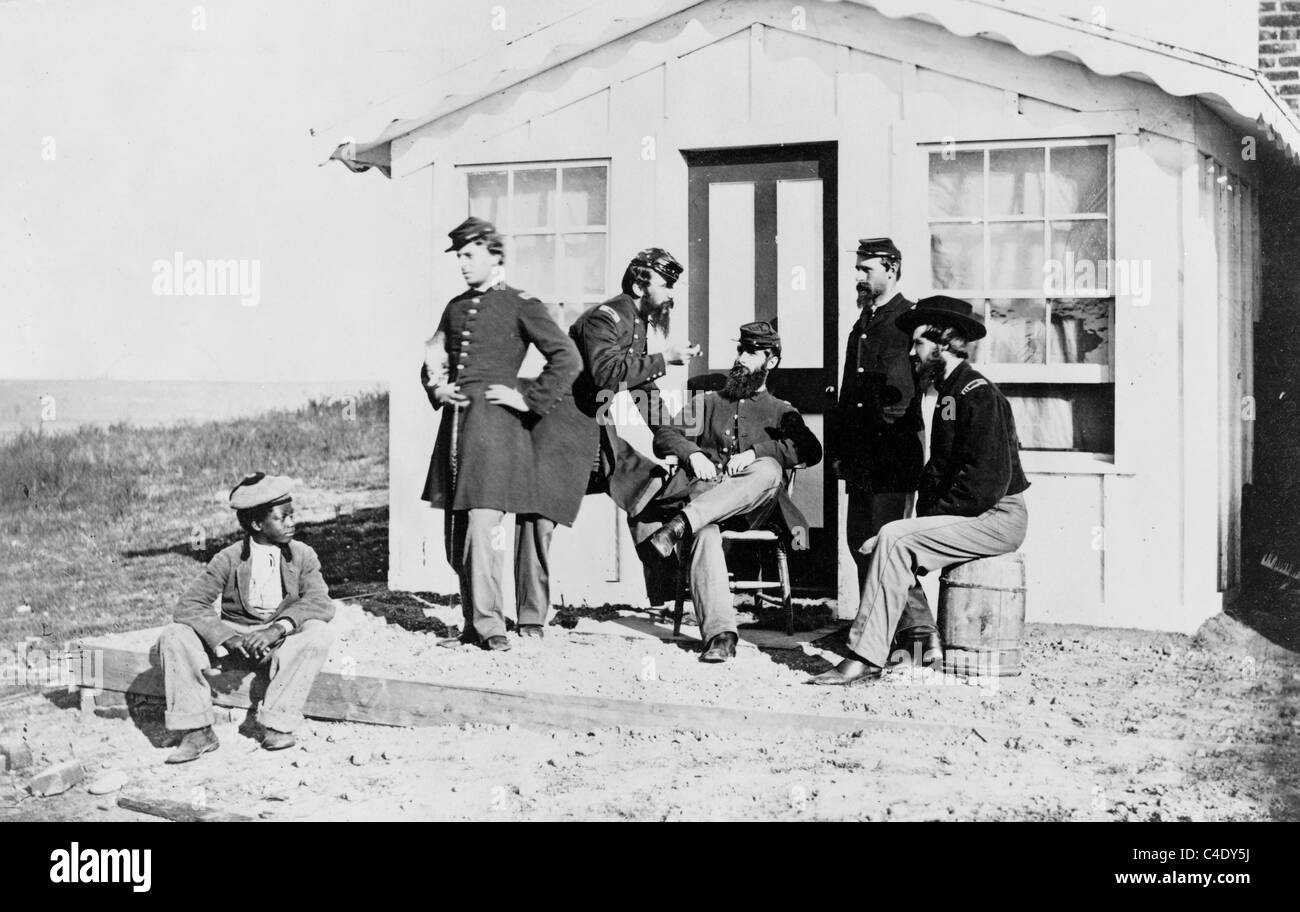 Five Civil War soldiers gathered on dirt porch outside home, African American youth seated near them. Stock Photo
