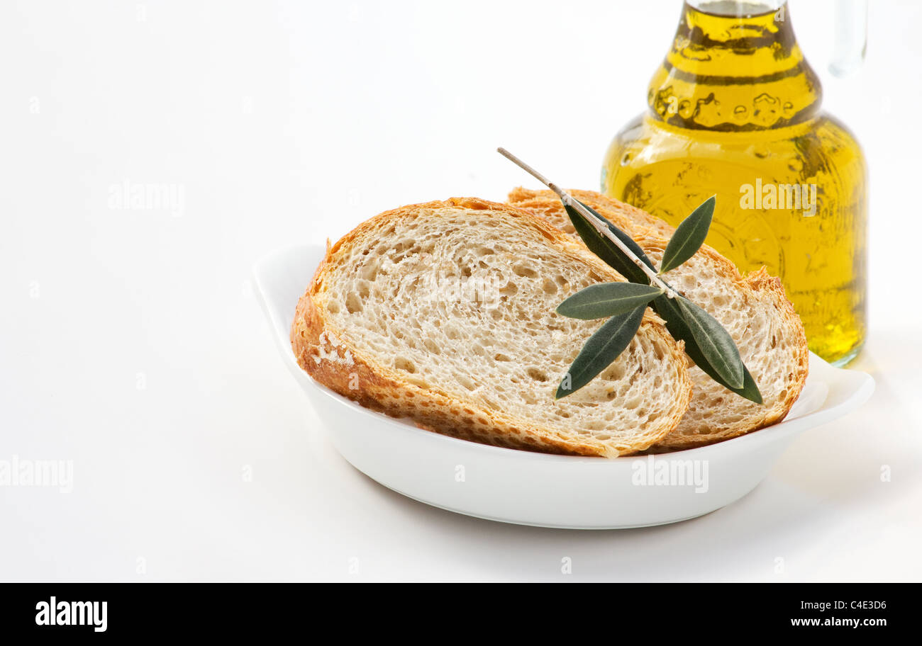 Close-up of slices of bread with olive leaves and bottle of olive oil on white background Stock Photo