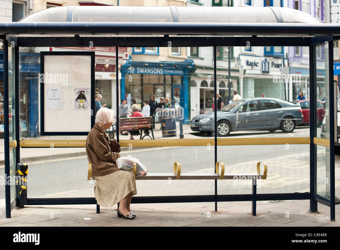 An Elderly Senior Woman Sitting Alone In A Bus Shelter Waiting For