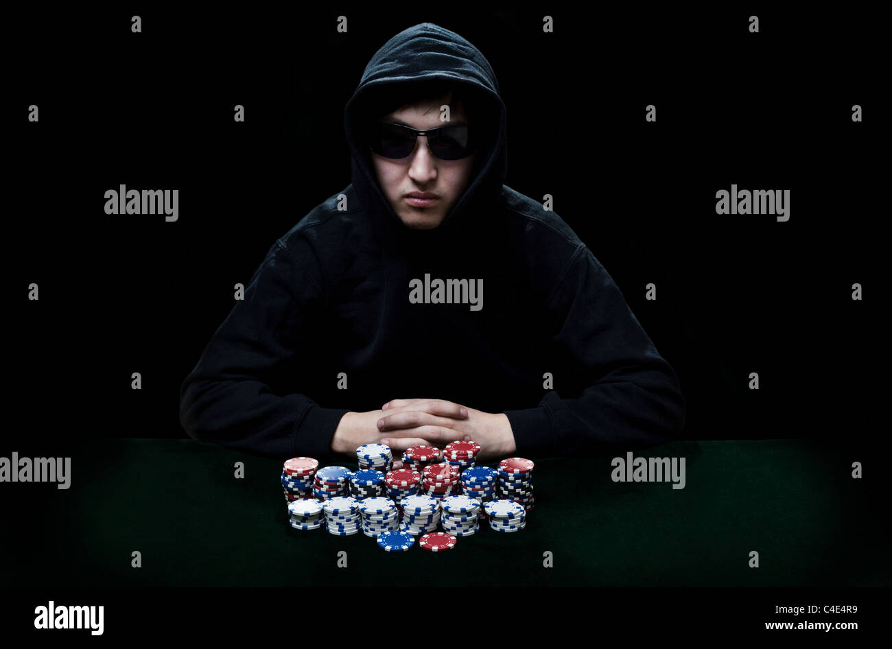 The guy in dark glasses, the player in gamblings sits at a table before it a heap poker chips Stock Photo