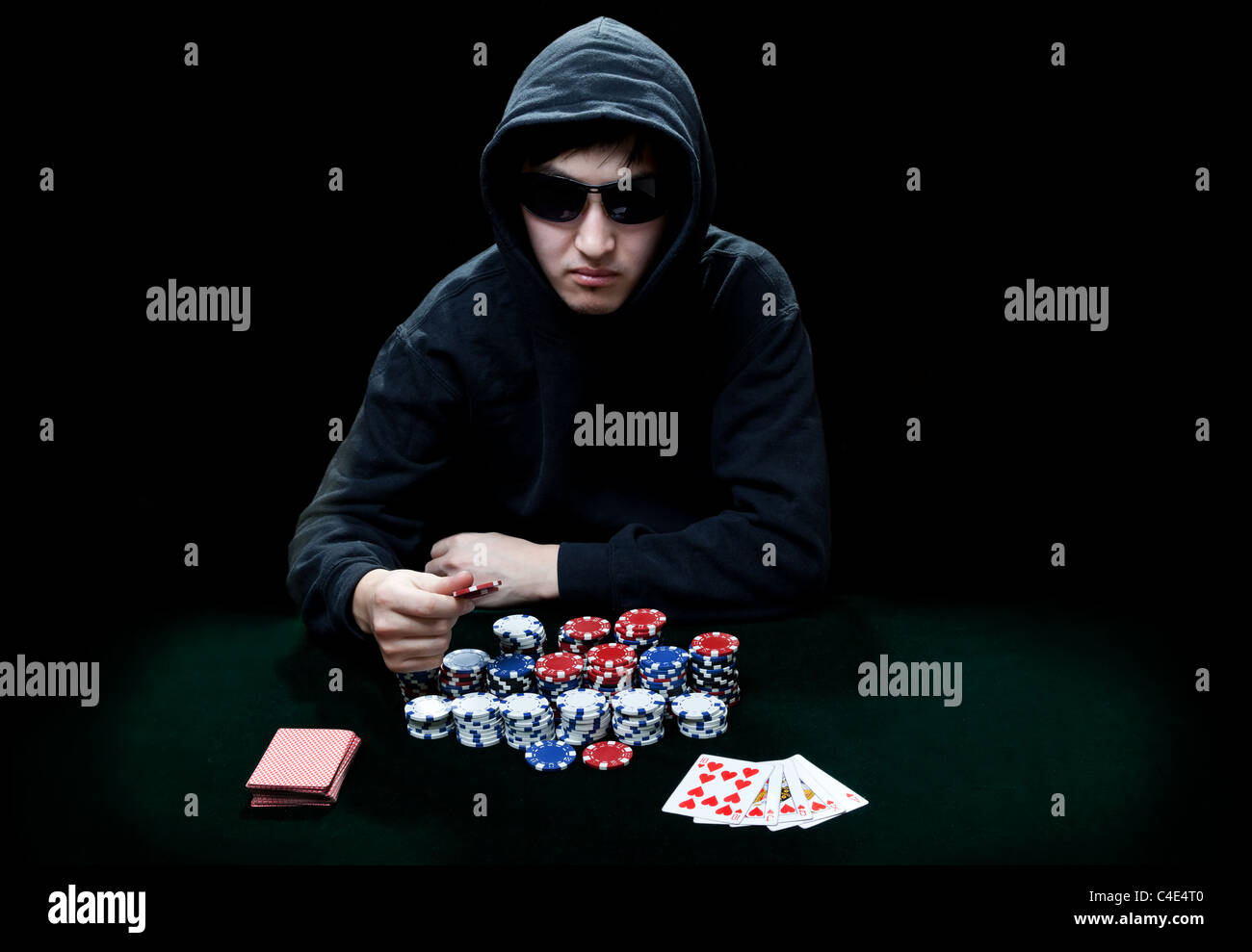 The guy in dark glasses, the player in gamblings sits at a table before it a heap poker chips Stock Photo