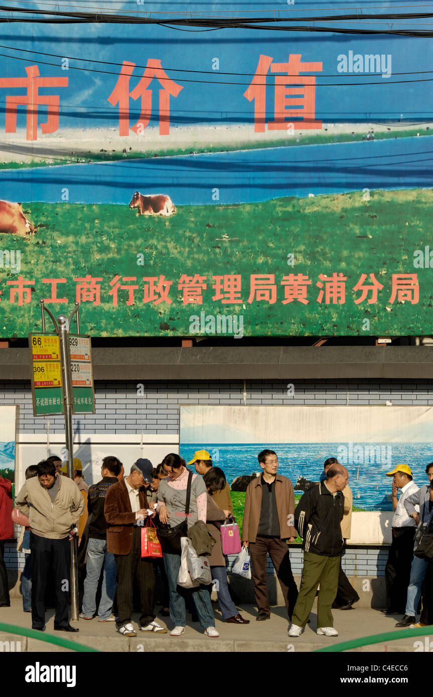 People waiting for buses in front of billboards erected around a building site, downtown Shanghai near the Bund, China. Stock Photo