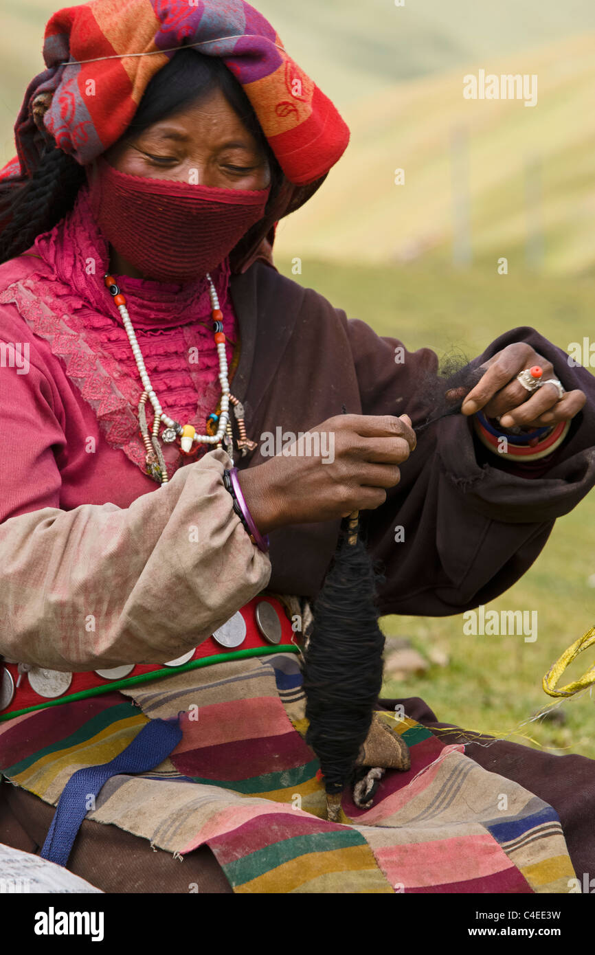 A Khampa nomad woman twists black yak hairs into a thread. The rough belly hairs are woven into tents and blankets. Sichuan Stock Photo