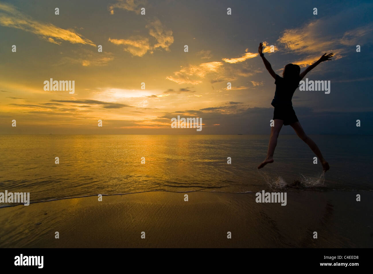 A young jumping for joy and enjoying her freedom on the beach at sunset. Taken on Phra Ae Beach, Koh Lanta, Thailand Stock Photo
