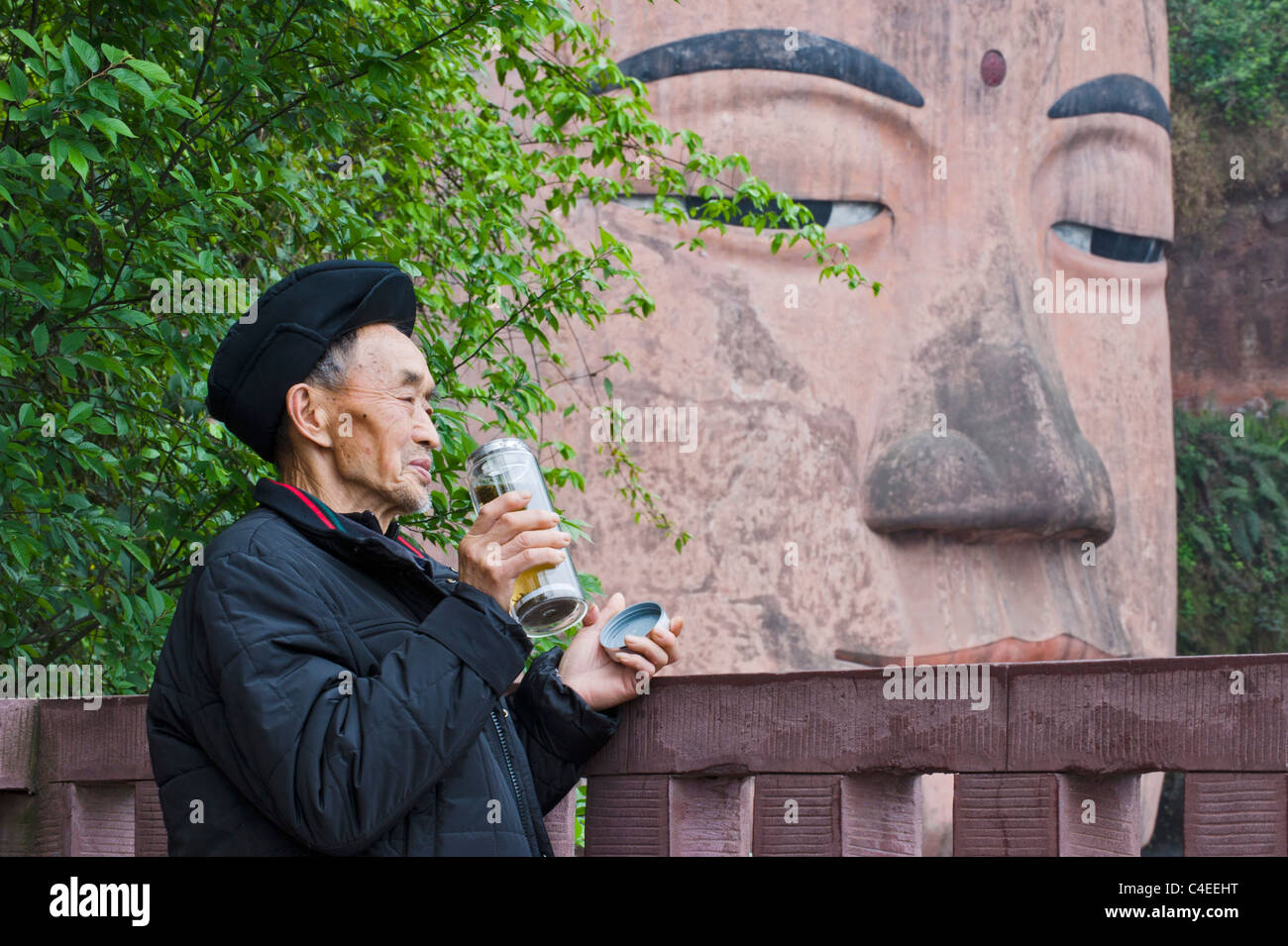 Man drinking tea by the 71-metre Giant Buddha of Leshan, the largest stone carved Buddha image in the world. Sichuan, China Stock Photo