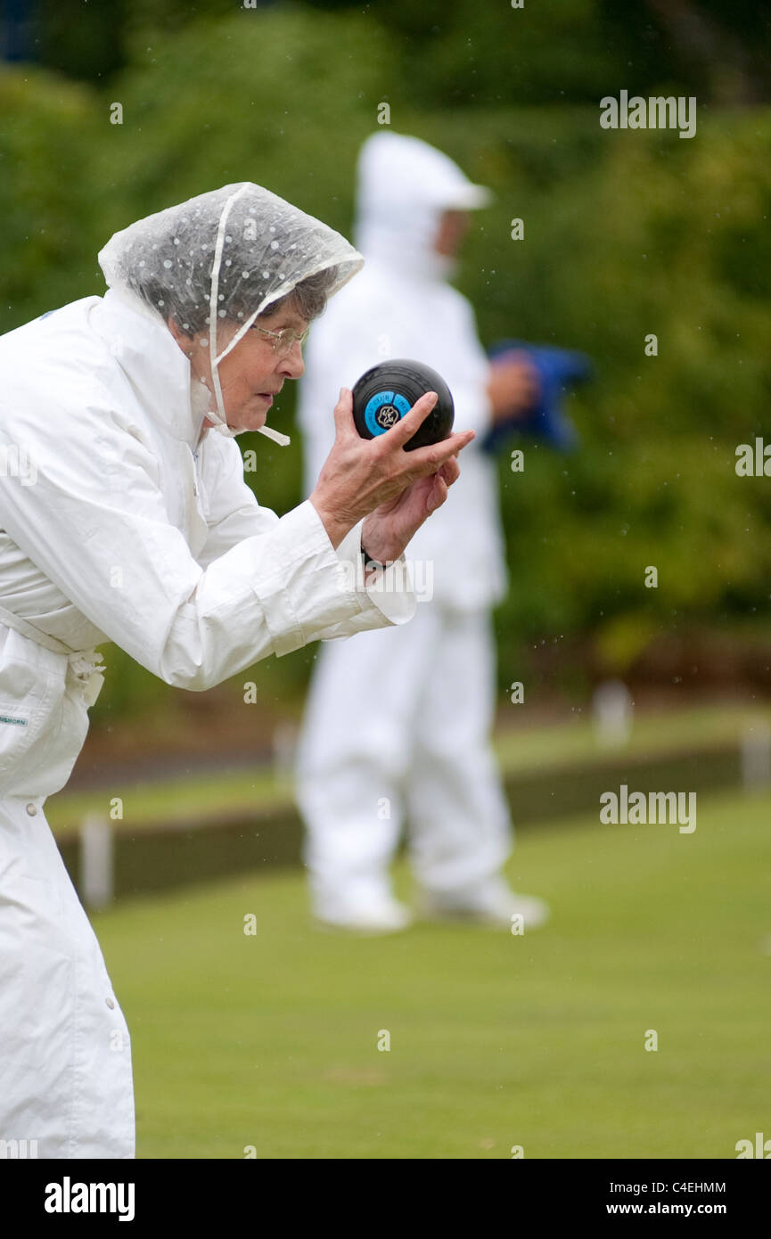 An active female pensioner takes part in a Sunday afternoon Lawn Bowls match in the rain Stock Photo