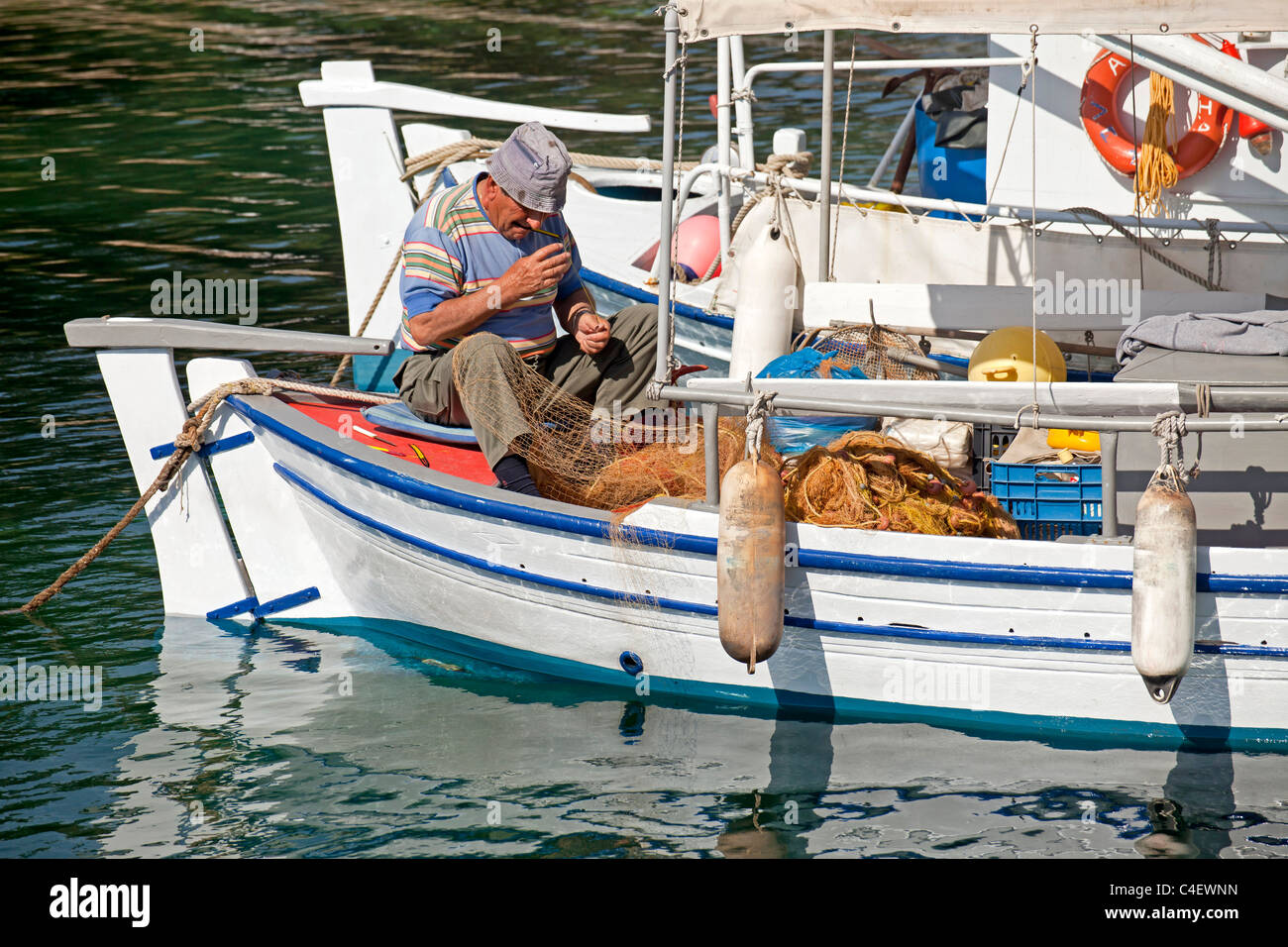 fisherman repairing his net on a boat at the old harbour of Skiathos Town, Skiathos Island, Northern Sporades, Greece Stock Photo