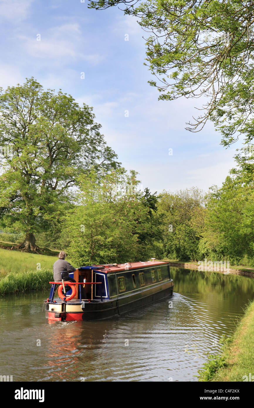 A man steers his canal narrow boat along the Leeds and Liverpool canal near Skipton, Yorkshire, England, UK Stock Photo
