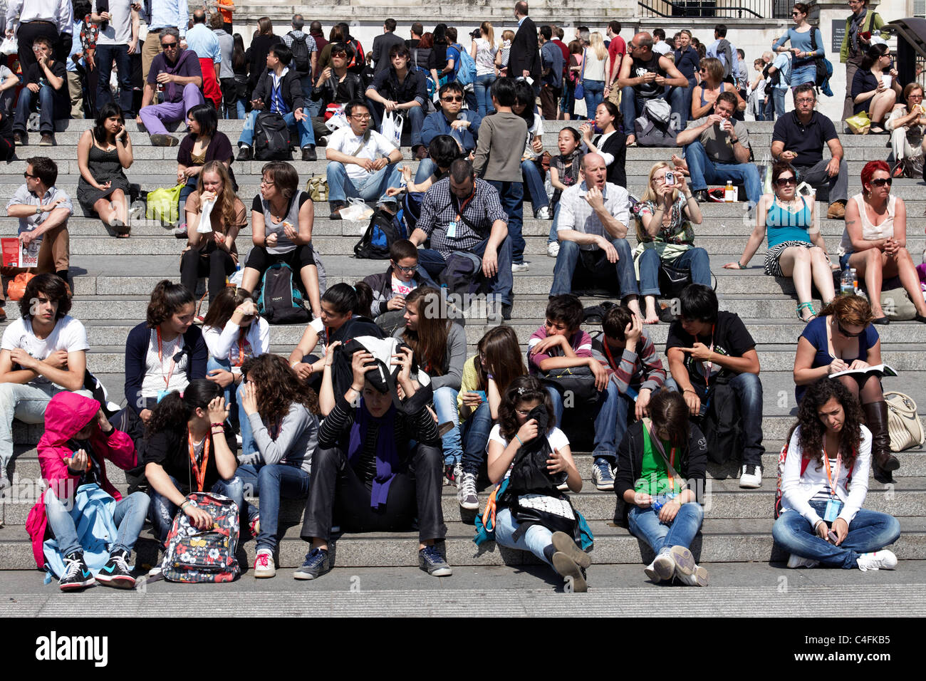 Tourists and Londoners  sitting on the steps in Trafalgar Square enjoy the sun on the hottest day of the year so far Stock Photo