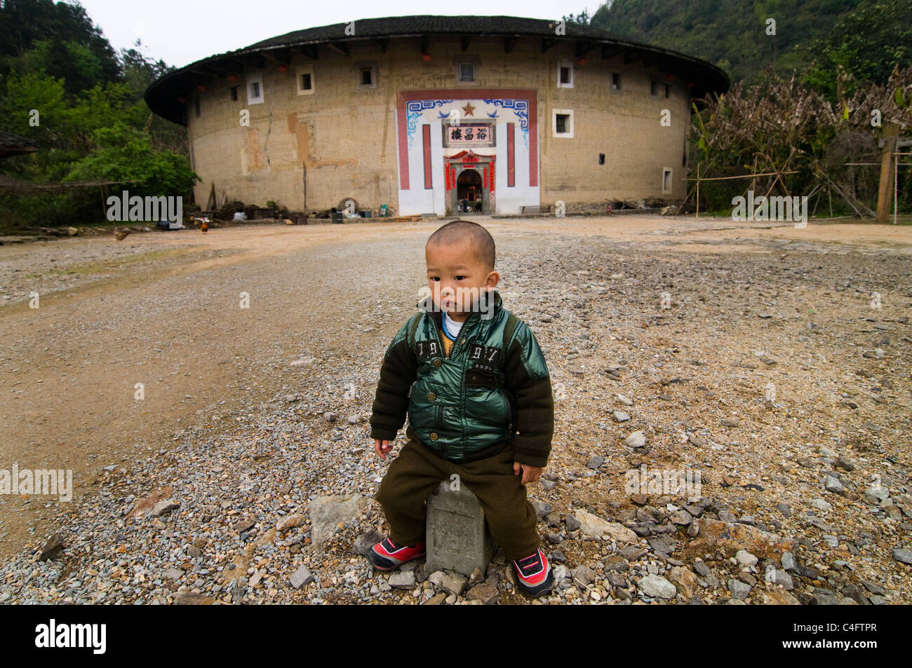 A Hakka boy standing in front of a big Tulou  building in Fujian. Stock Photo
