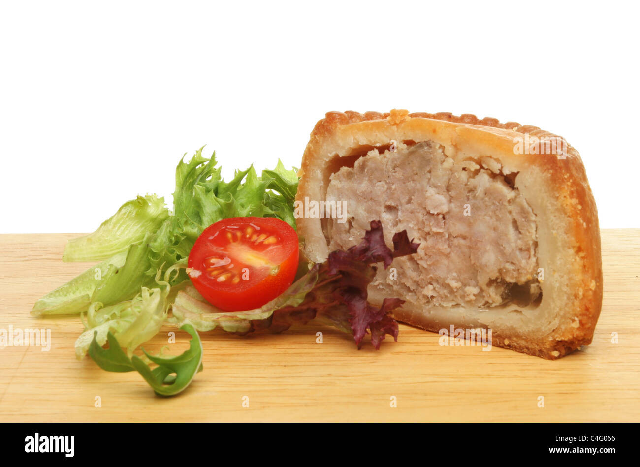 A portion of pork pie with salad garnish on a wooden food preparation board Stock Photo