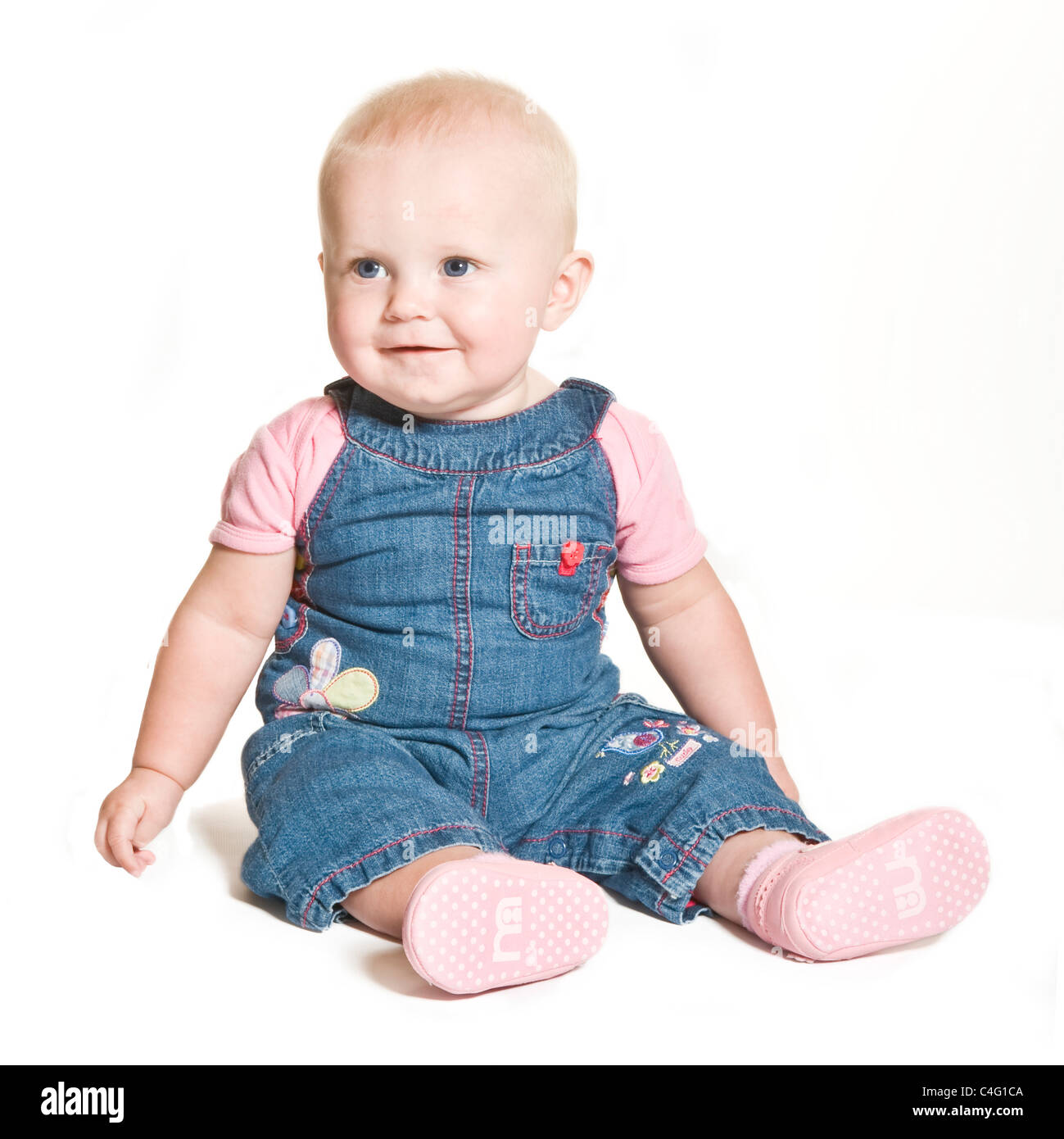 A cute 1 year old baby girl with blue eyes wearing denim and pink smiling against a pure white (255) background. Stock Photo