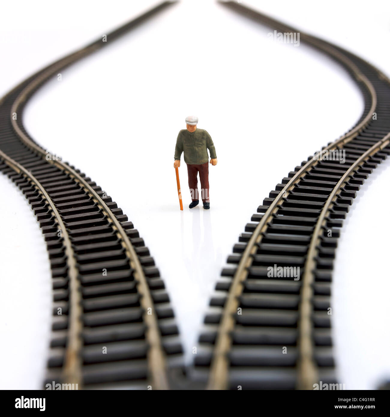 Miniature elderly figure standing at a crossroads of toy train tracks ...