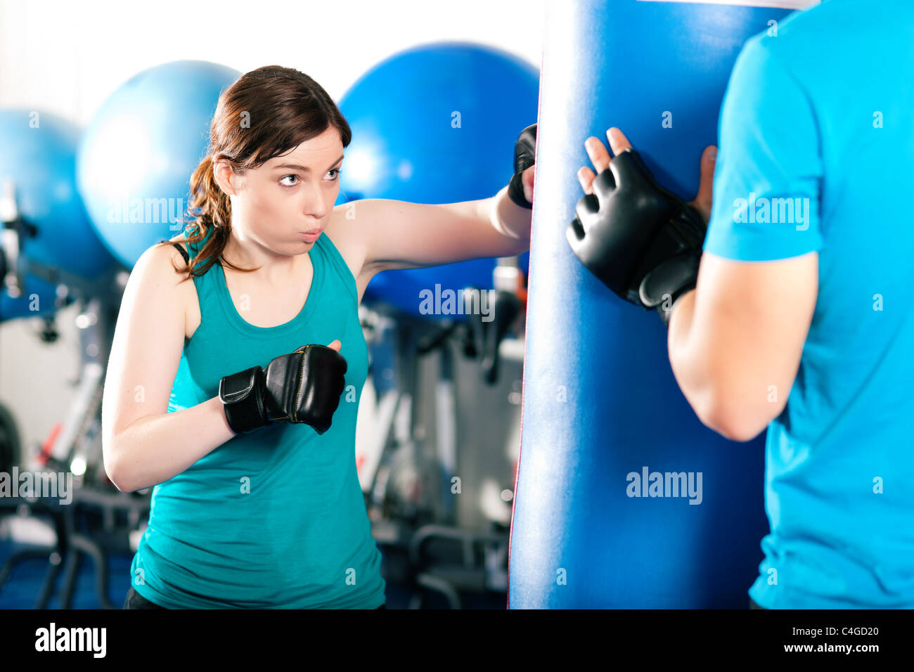 Woman Boxer hitting the sandbag, her trainer is assisting Stock Photo