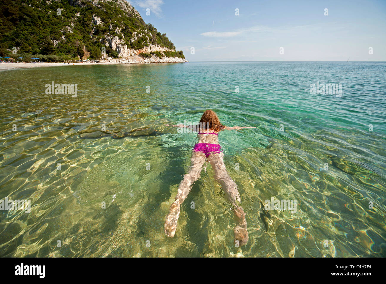 young woman with pink Bikini swimming in the clear water of Limnonari