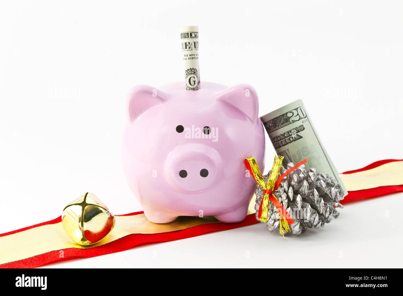 Pink bank shaped like a pig is placed with currency, silver pine cone, and holiday ribbon with bells. Stock Photo