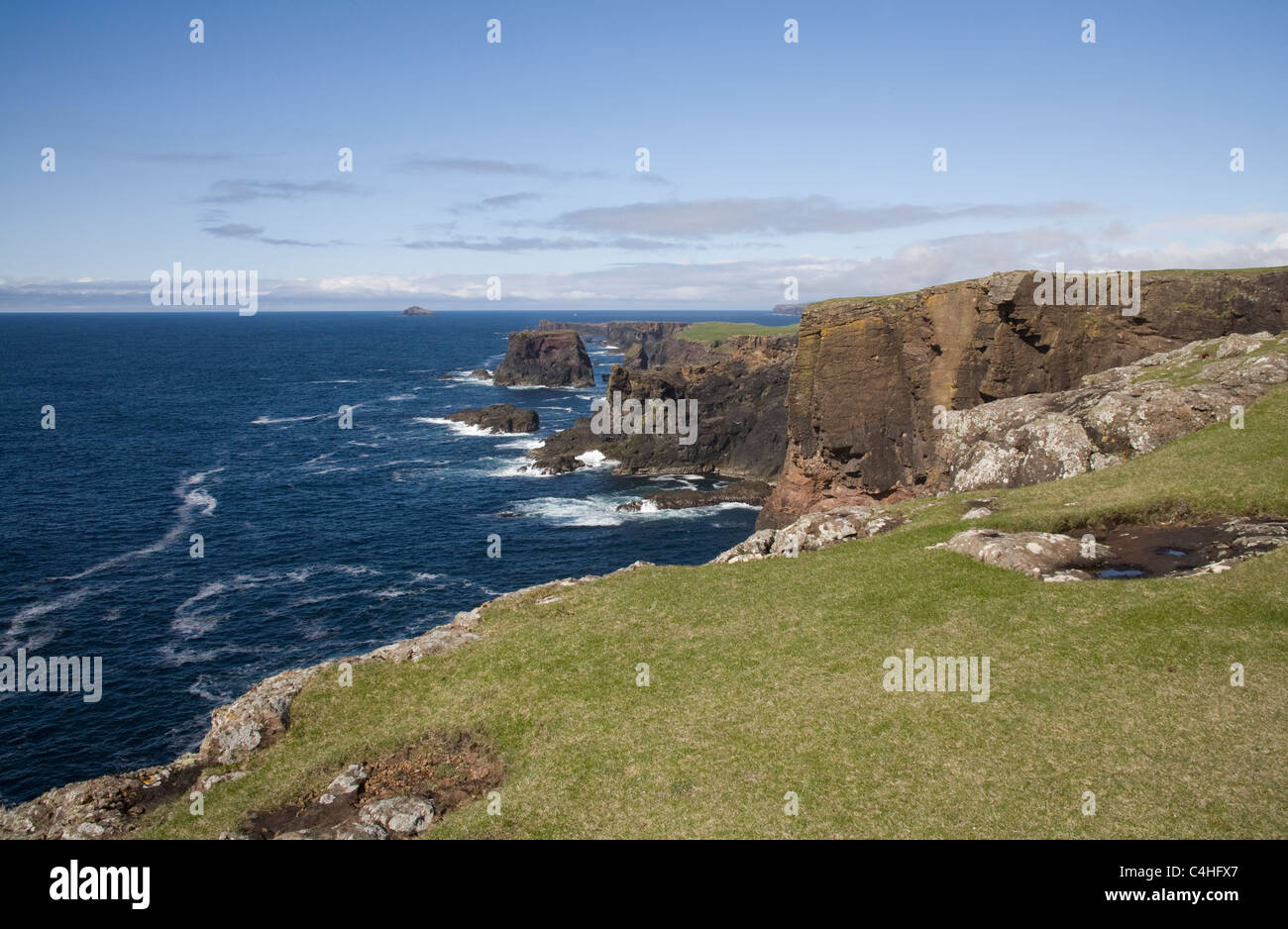 Eshaness Shetland Isles Grassy headland above dramatic red sandstone cliffs caves and stacks of the Northmavine coastline Stock Photo