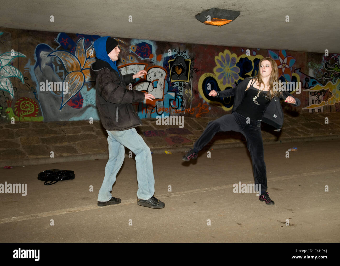 Scene showing young Caucasian woman defending herself with tae kwon doong martial arts against attacker in underpass in Bristol Stock Photo
