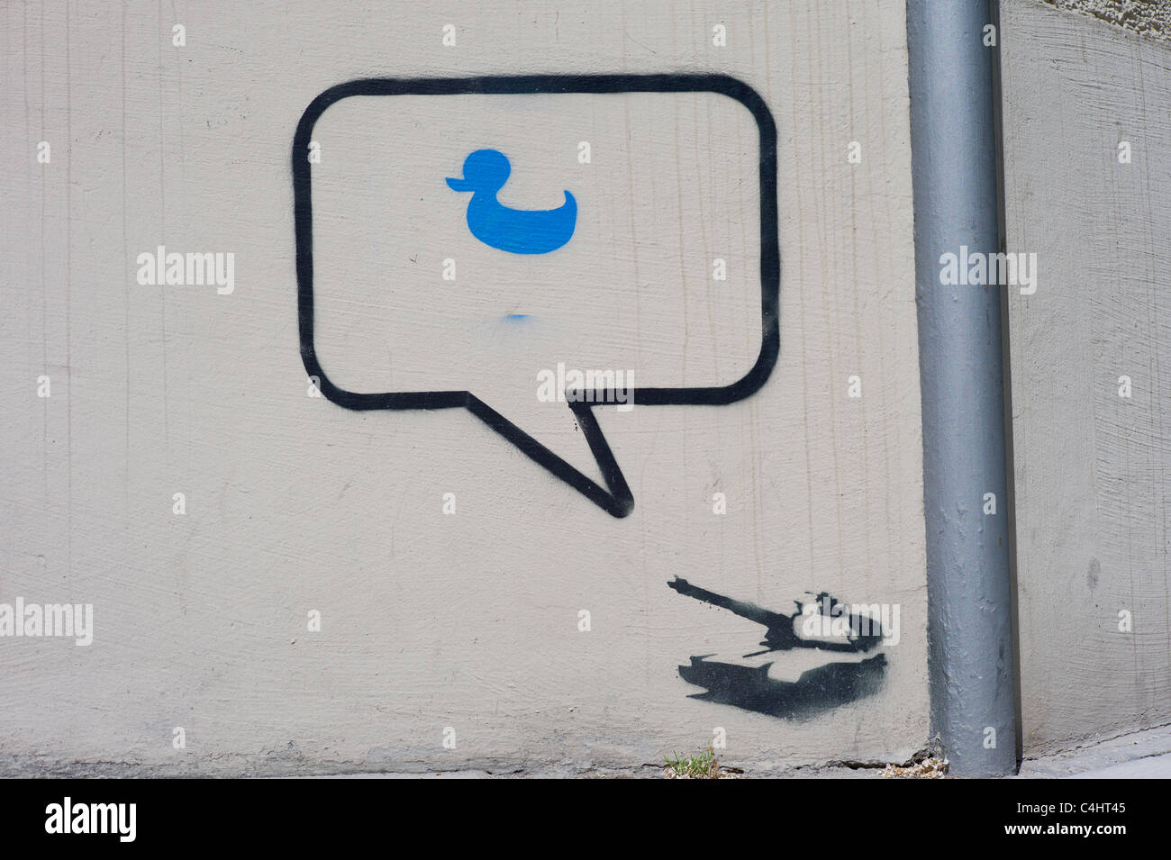 Stencil / graffito on a wall showing a  tank, a speech bubble next to the gun and a blue duck located inside the bubble Stock Photo