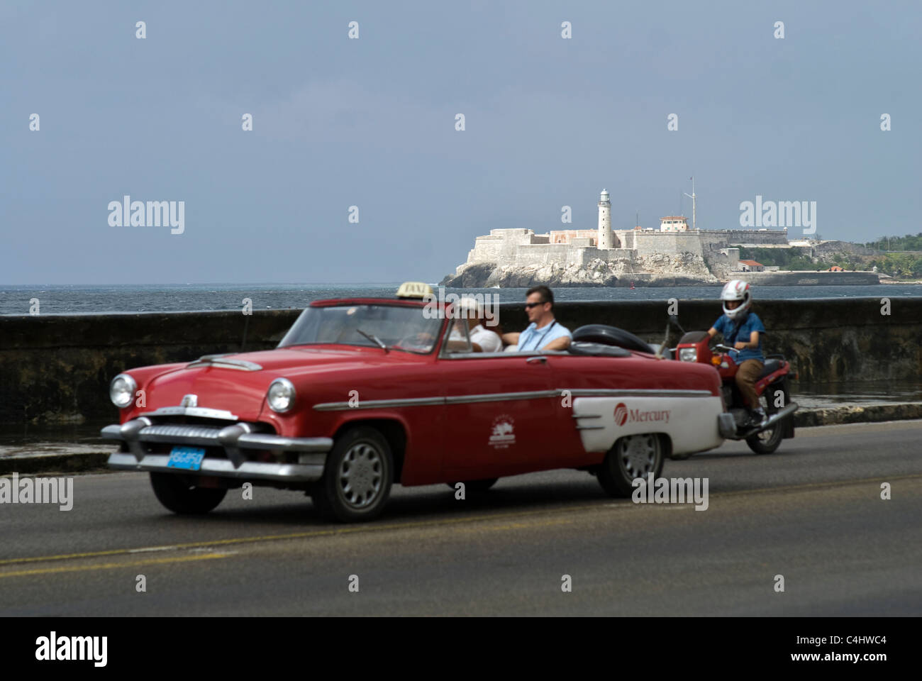 Ford Mercury taxi in drives along the Malecon in Havana, Cuba with a lighthouse in the background. © Craig M. Eisenberg Stock Photo