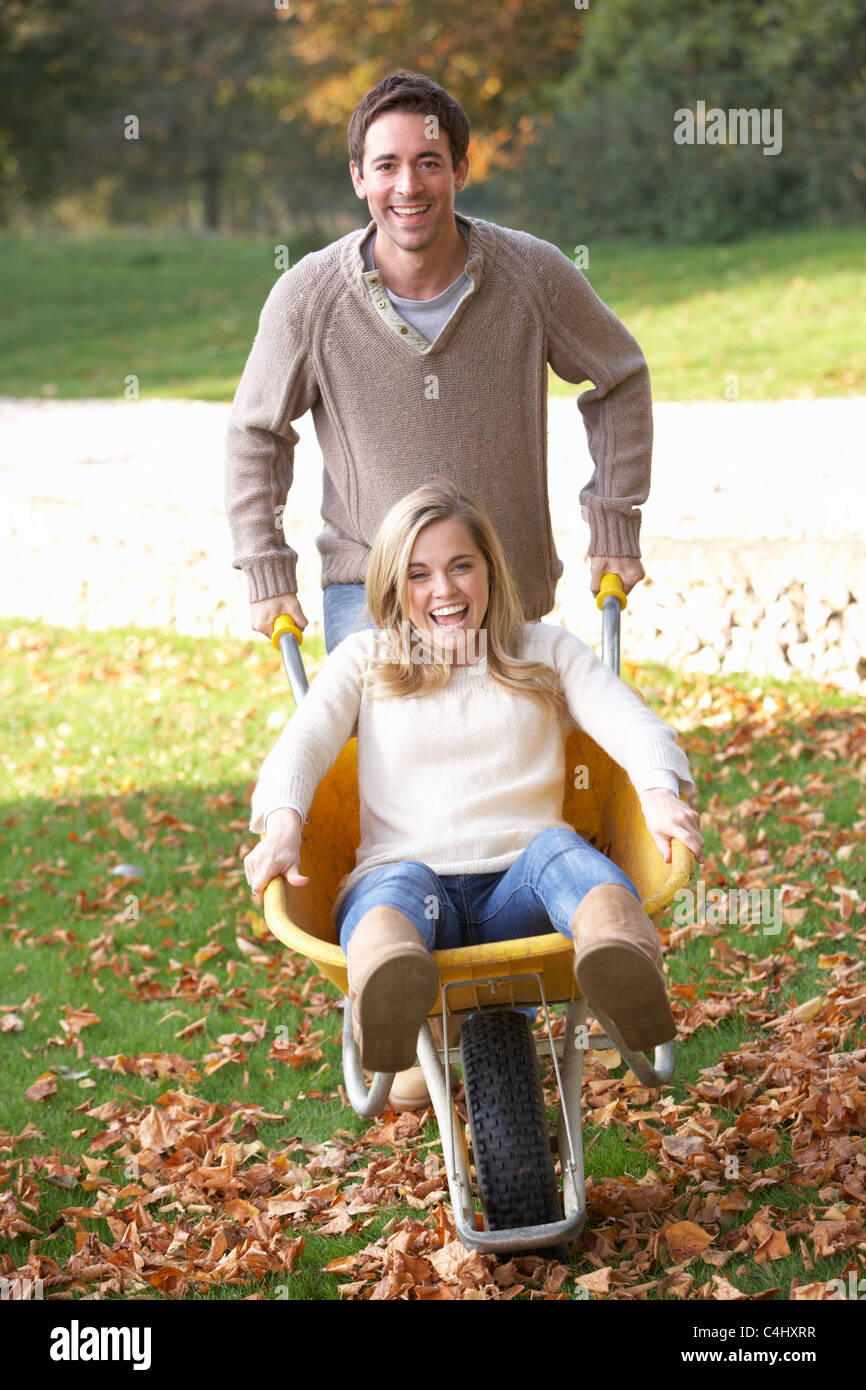 Man pushing wife through autumn leaves on wheelbarrow Stock Photo