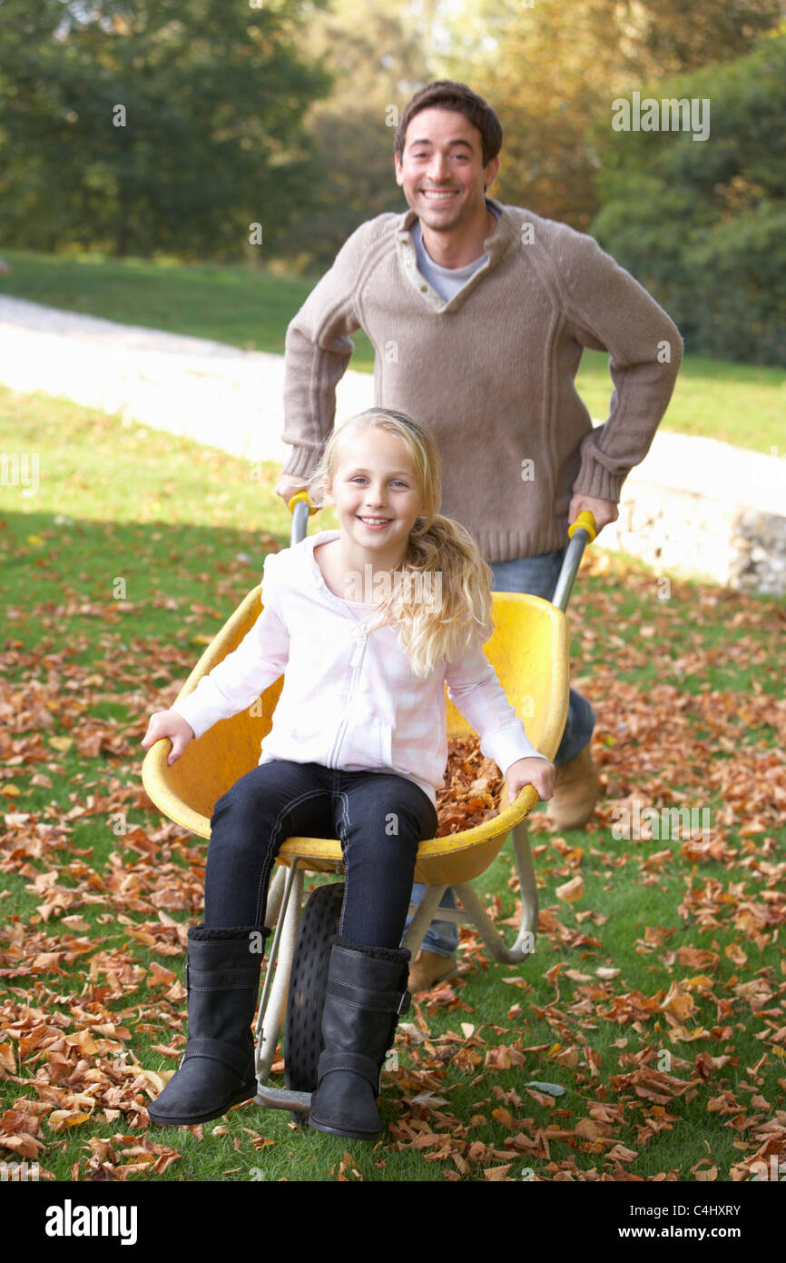 Father pushing child through autumn leaves on wheelbarrow Stock Photo
