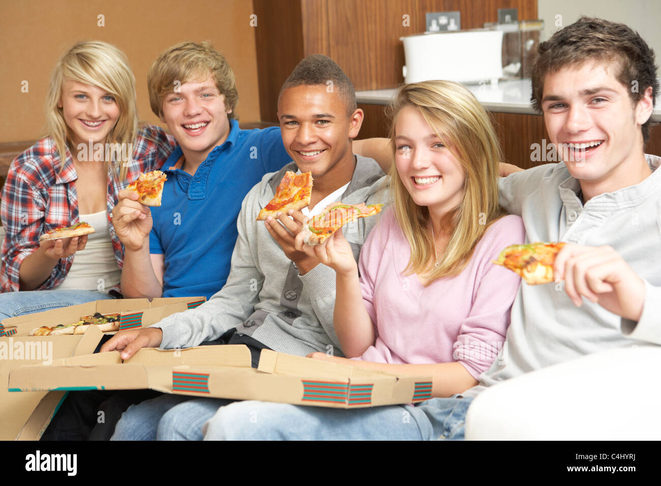 Group Of Teenage Friends Sitting On Sofa At Home Eating Pizza Stock Photo