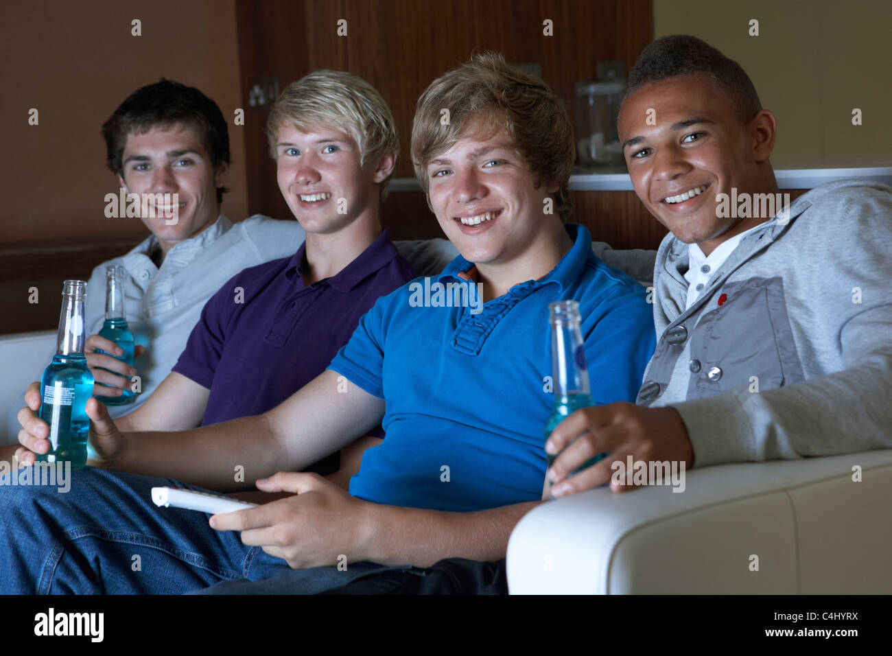 Group Of Teenage Boys Sitting On Sofa At Home Watching Drinking Alcohol Stock Photo