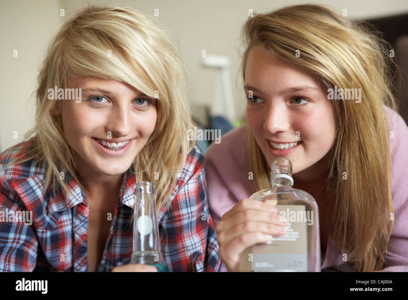 Two Teenage Girls Sitting On Sofa At Home Drinking Alcohol Stock Photo