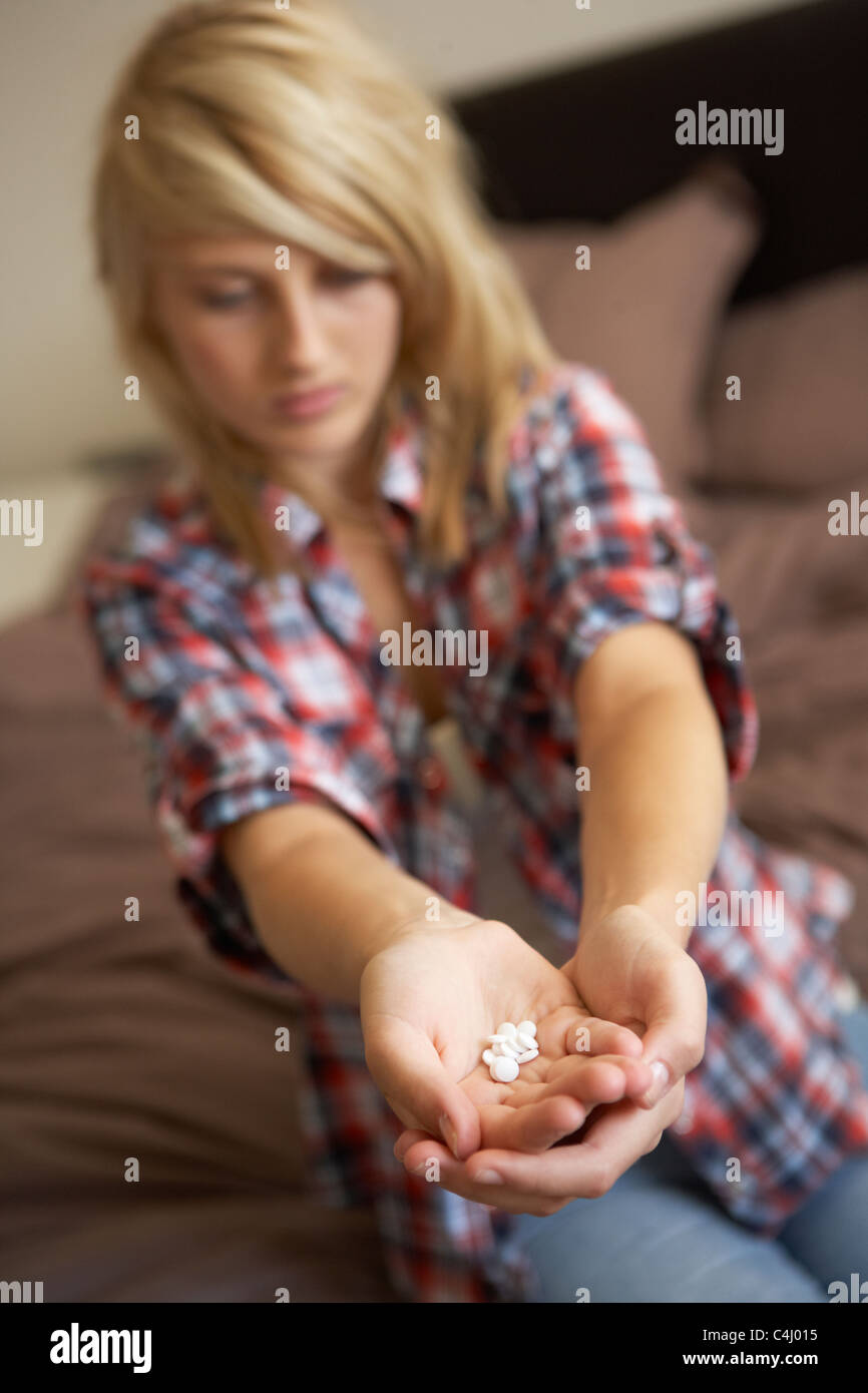Depressed Teenage Girl Sitting In Bedroom With Pills Stock Photo