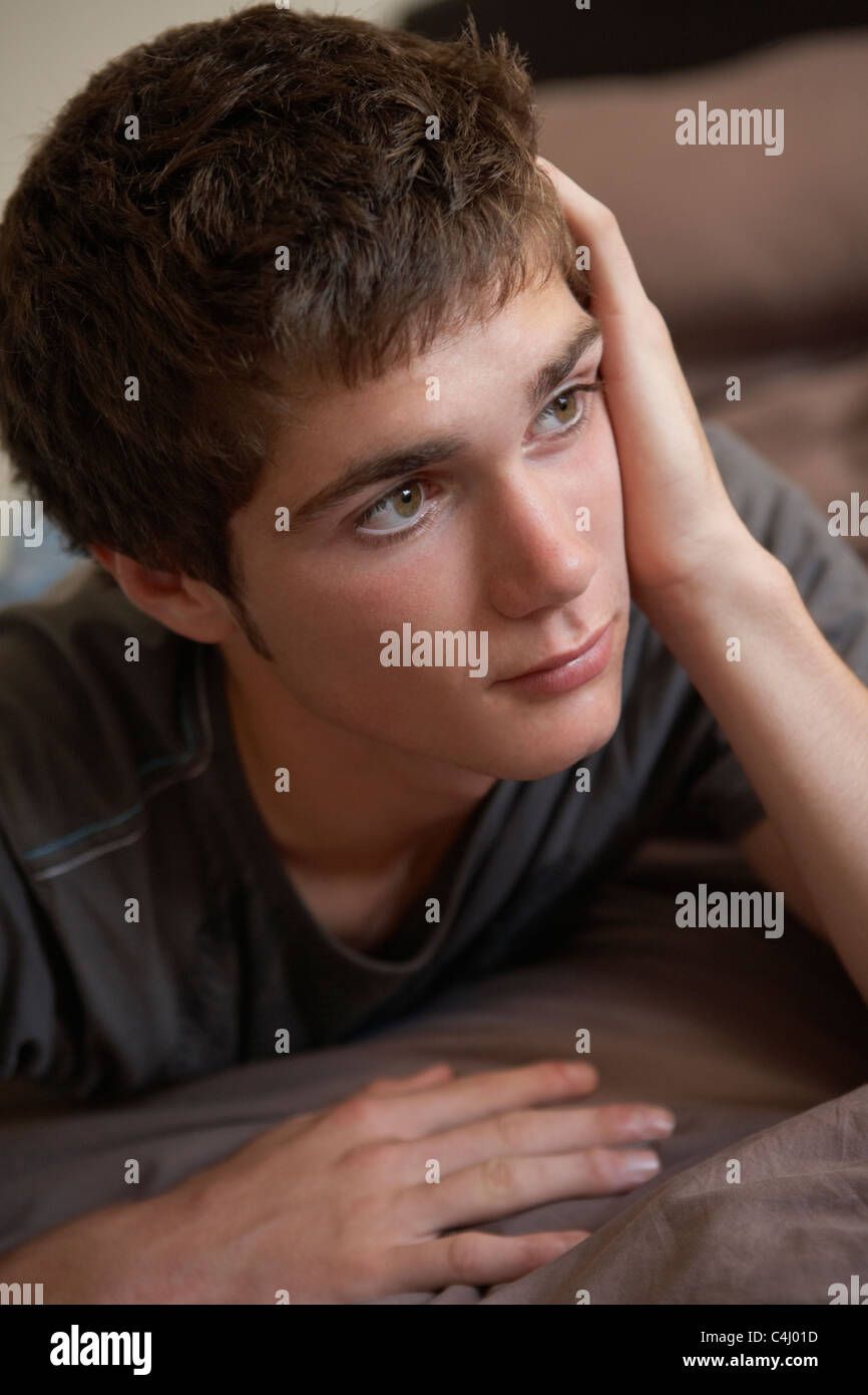 Depressed Teenage Boy Lying In Bedroom Stock Photo