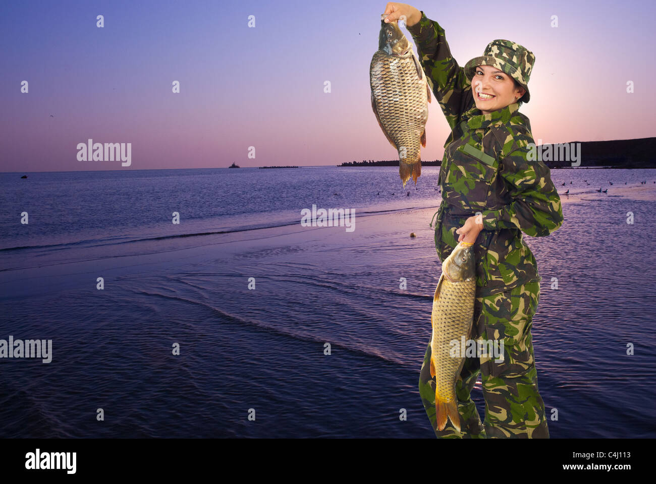 Happy fisherwoman at lake walking and holding two big carps in the morning at sunrise,copy space for text message Stock Photo
