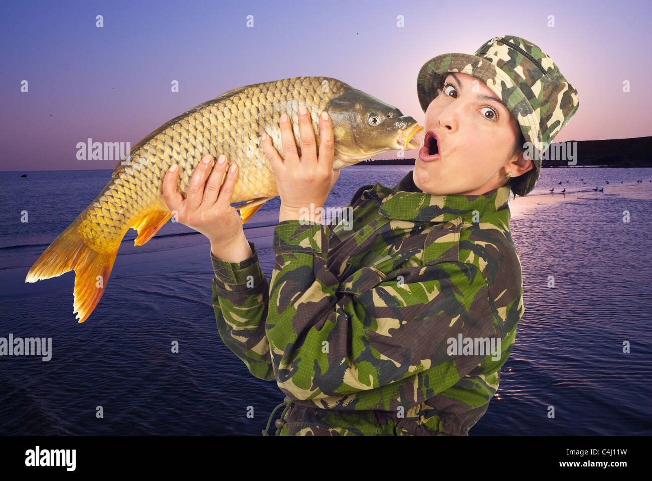 Funny angler woman holding and mimic a big fish at lake in the