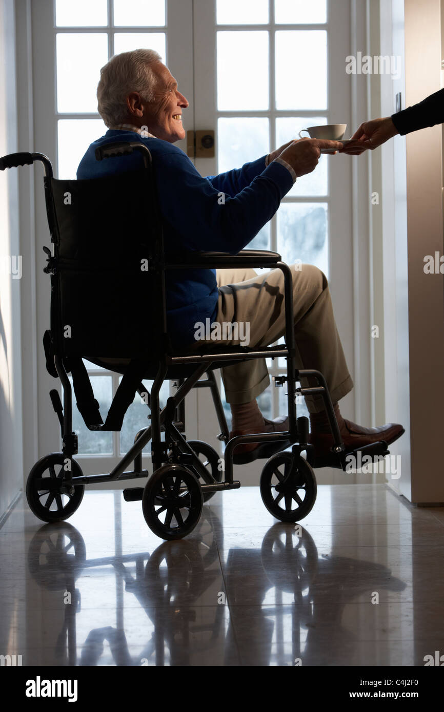 Disabled Senior Man Sitting In Wheelchair Being Handed Cup Stock Photo