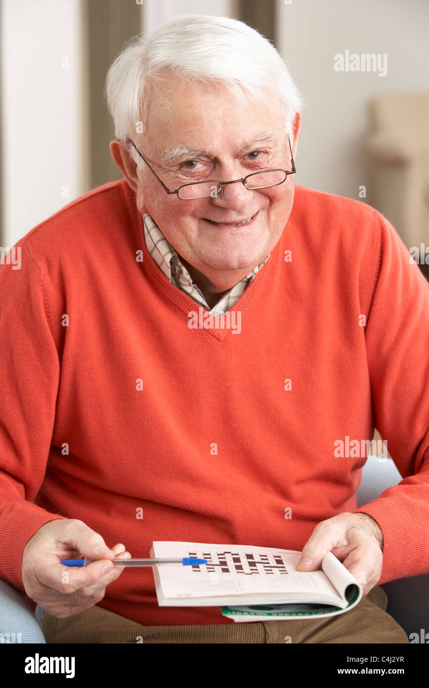 Senior Man Relaxing In Chair At Home Completing Crossword Stock Photo