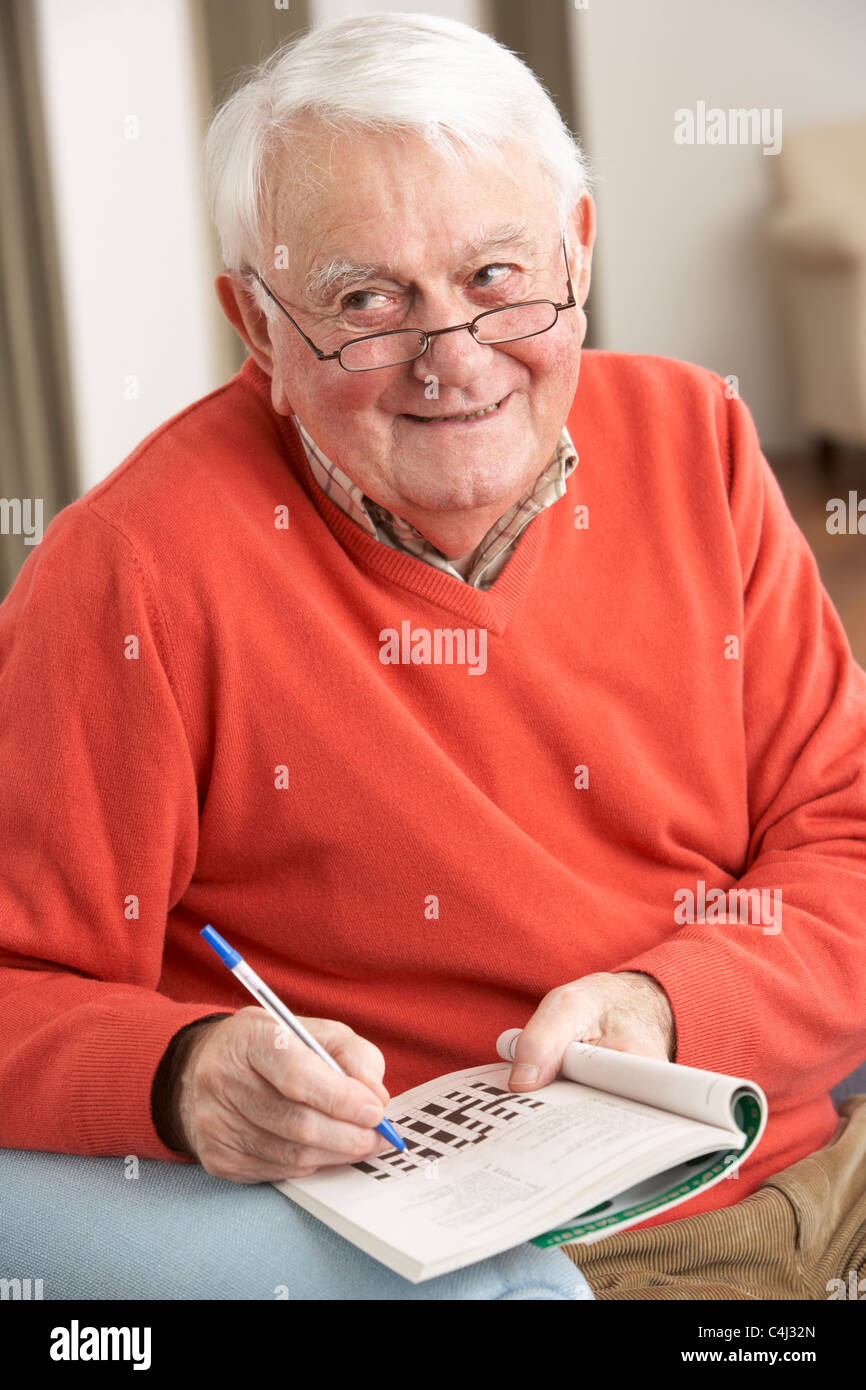 Senior Man Relaxing In Chair At Home Completing Crossword Stock Photo