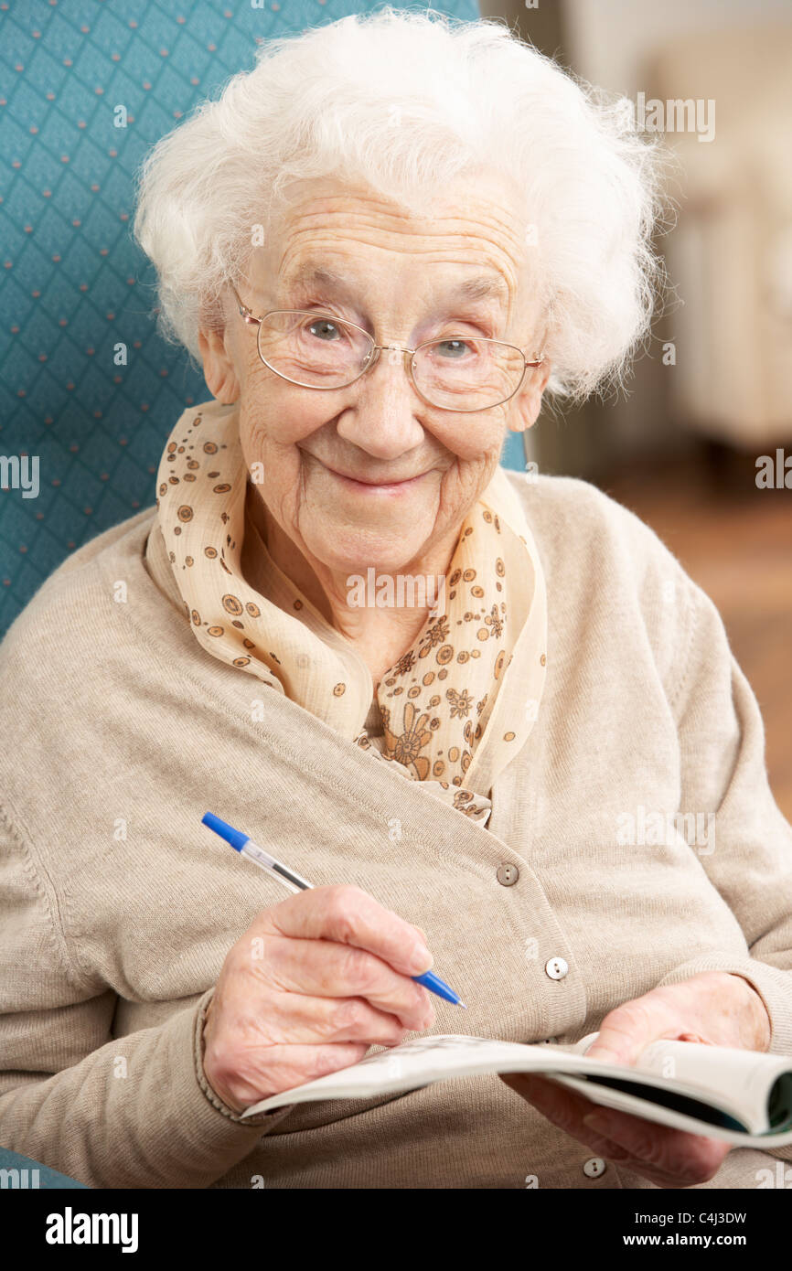 Senior Woman Relaxing In Chair At Home Completing Crossword Stock Photo