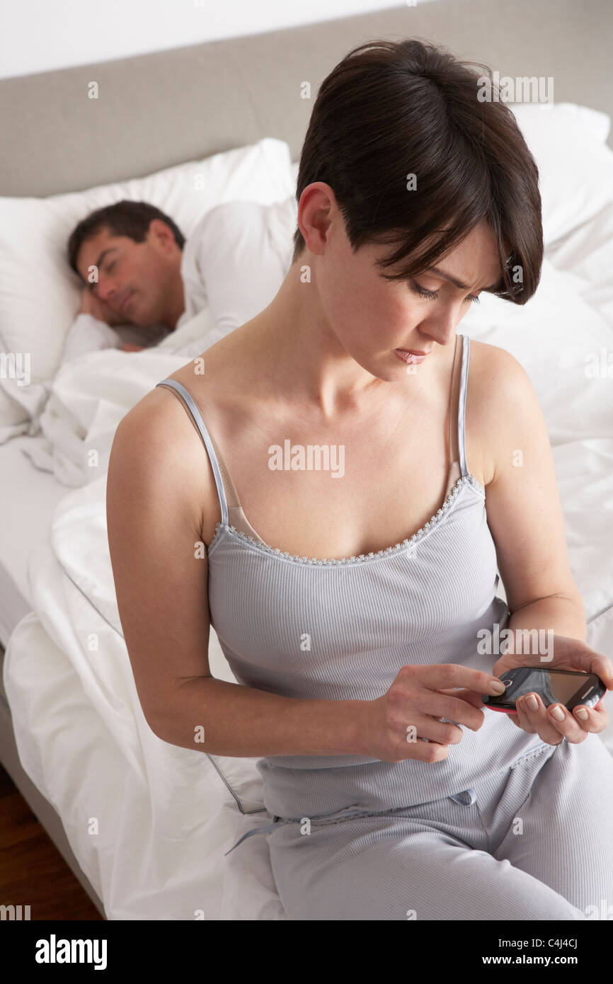 Suspicious Wife Checking Husband's Mobile Phone Whilst He Sleeps Stock Photo