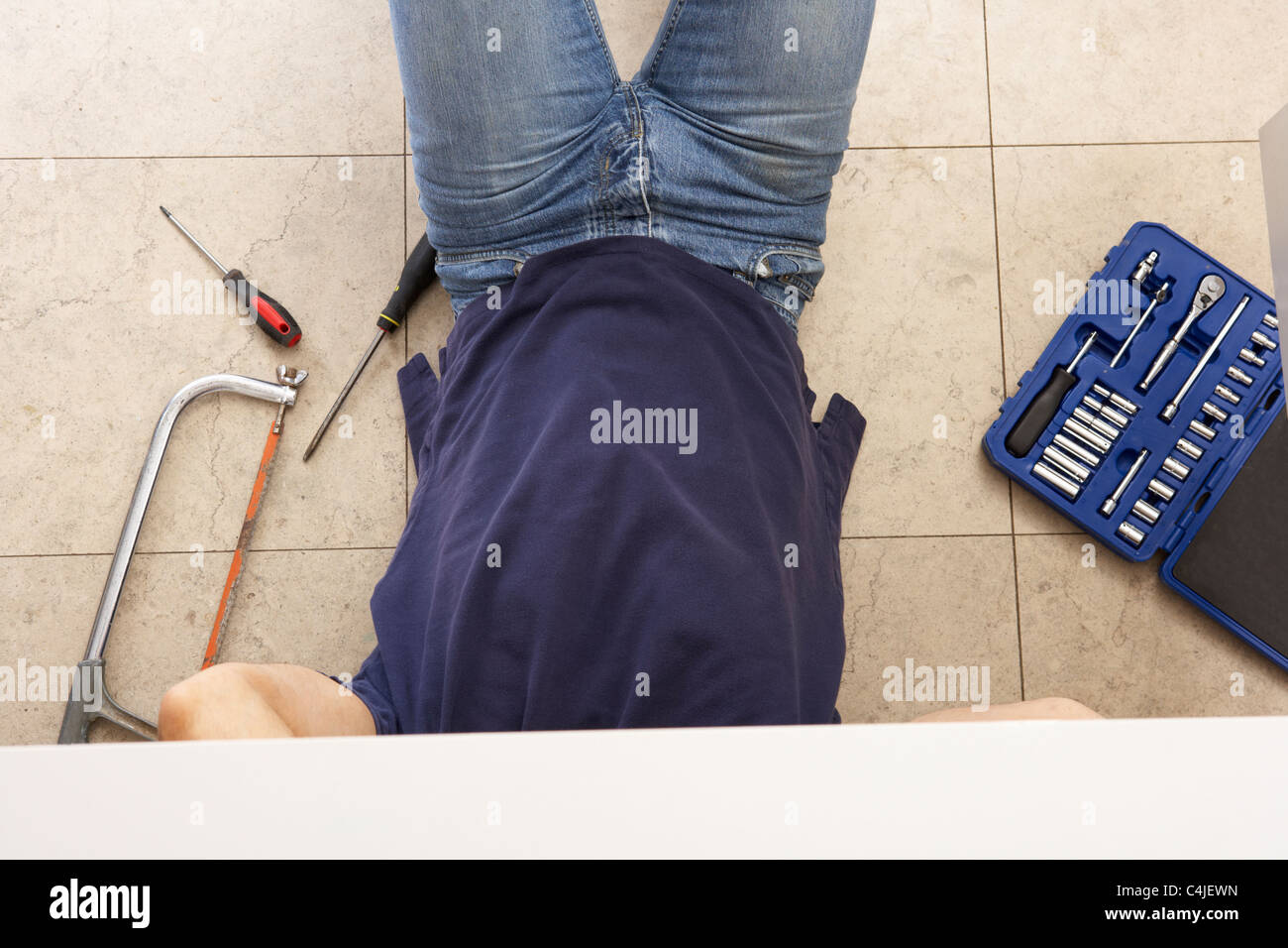 Plumber Working On Sink In Kitchen Stock Photo