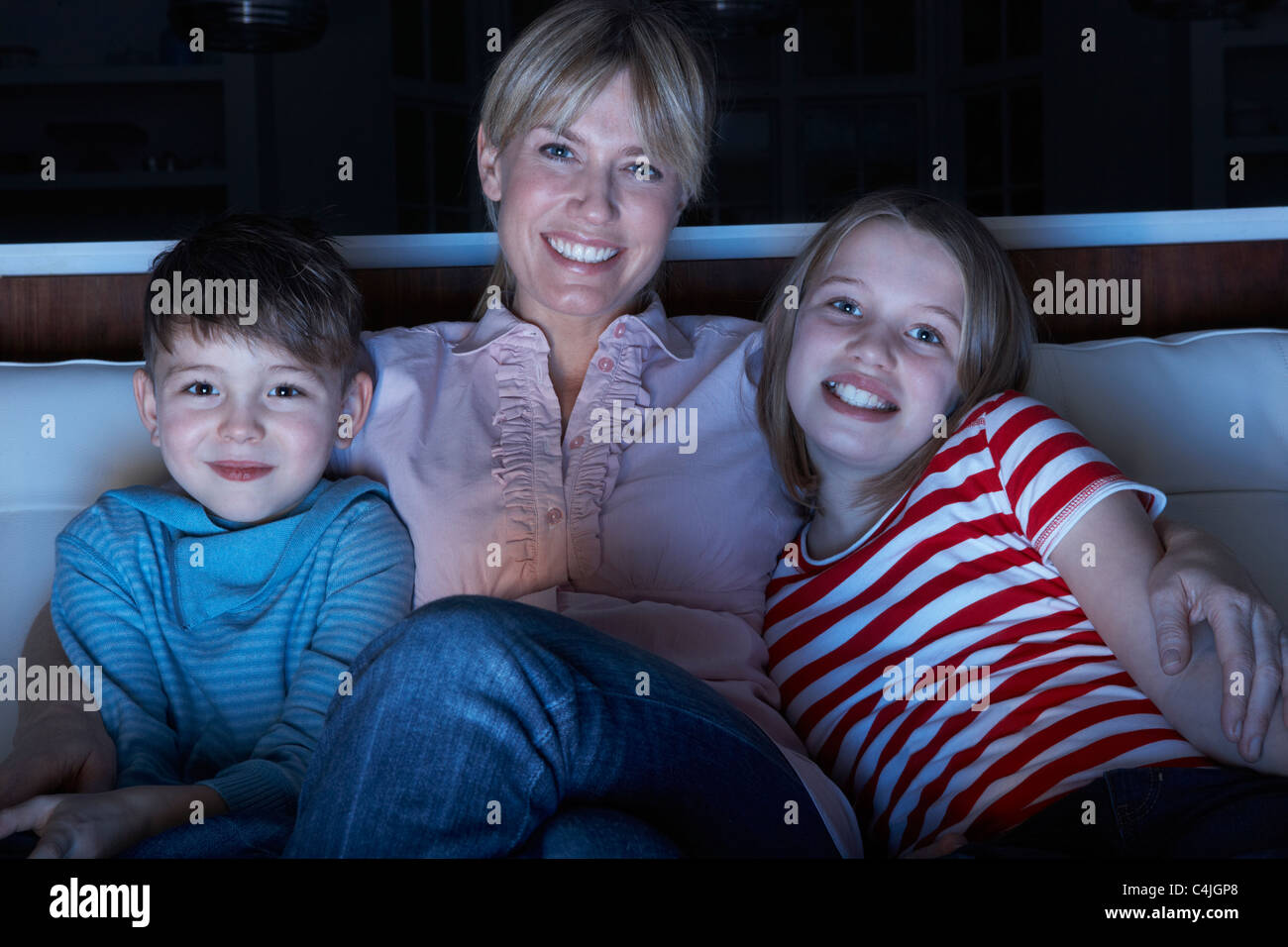 Mother And Children Watching Programme On TV Sitting On Sofa Together Stock Photo