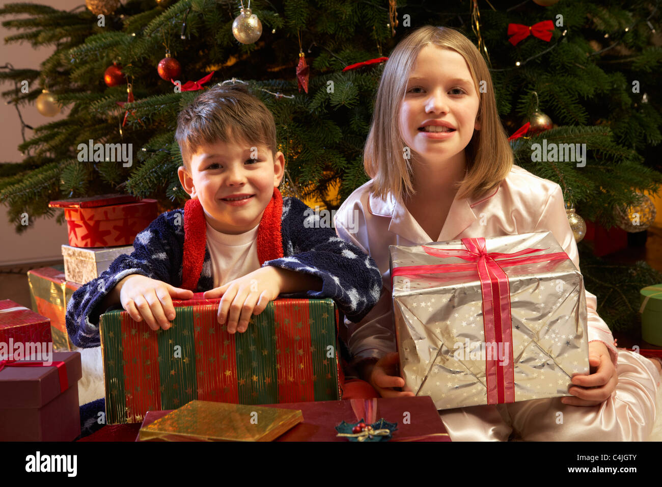 Children Opening Christmas Present In Front Of Tree Stock Photo