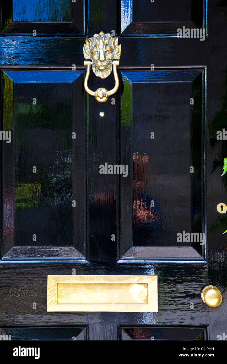 A shiny high gloss black painted front door with highly polished brass door furniture. Stock Photo