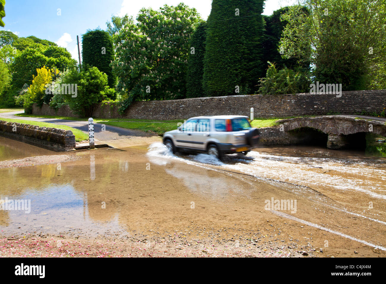 A four wheel drive crossing ford in pretty Cotswold village of Shilton, Oxfordshire, England, UK on a sunny day in early spring Stock Photo