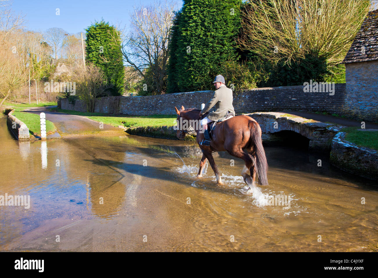 A horse and rider crossing ford in pretty Cotswold village of Shilton, Oxfordshire, England, UK on a sunny day in early spring Stock Photo