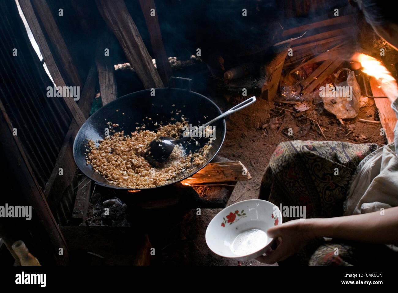 An Asian woman living in poverty is frying rice in a pan on a wood ...