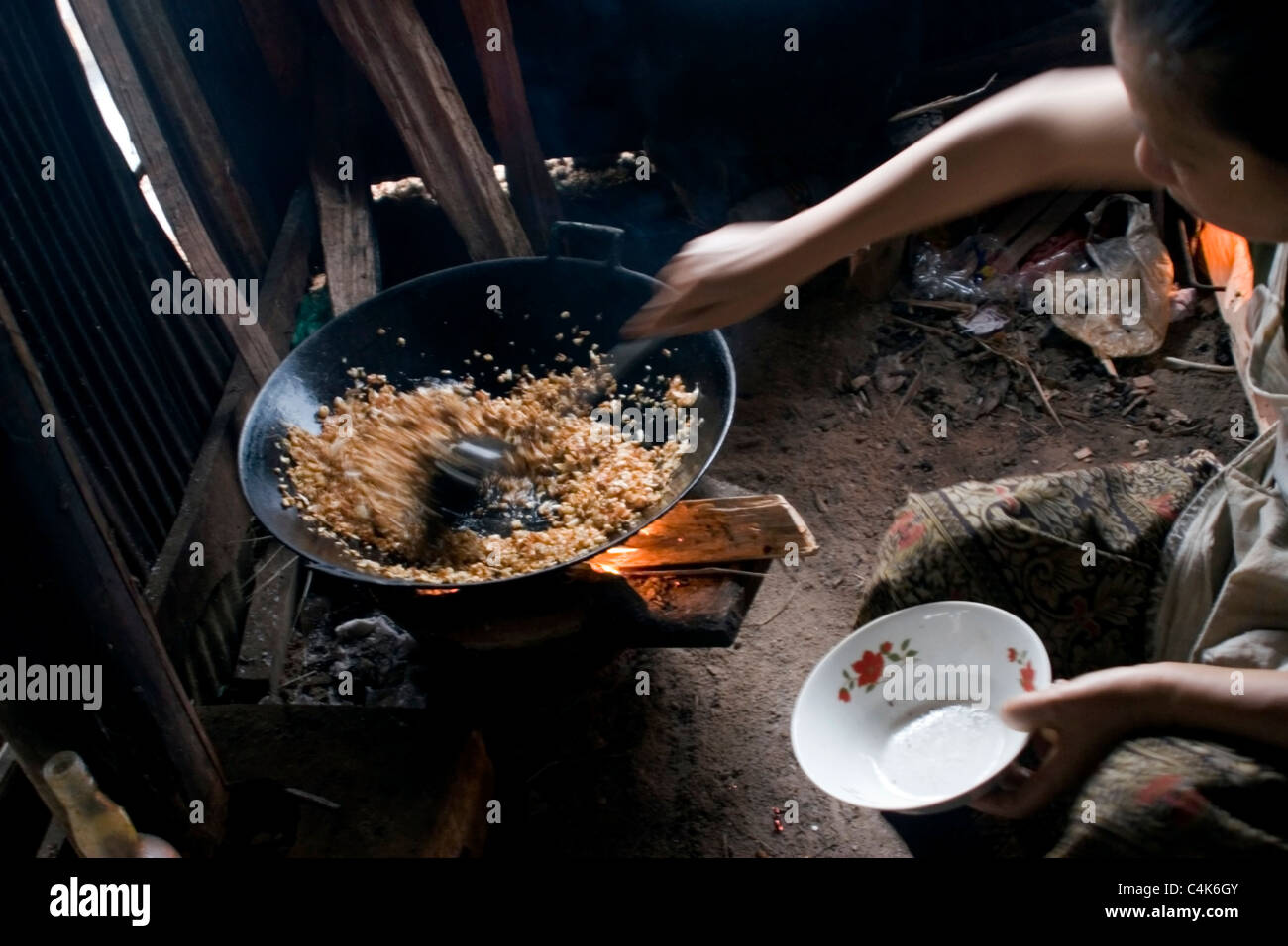 An Asian woman living in poverty is frying rice in a pan on a wood ...