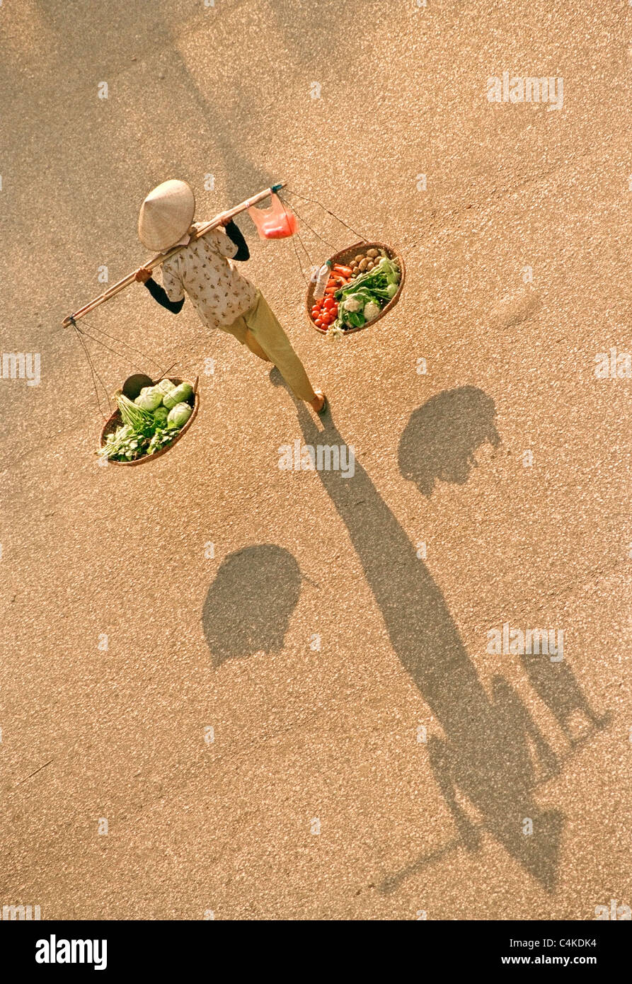 Vietnamese woman carrying trays of fruit and vegetables suspended from