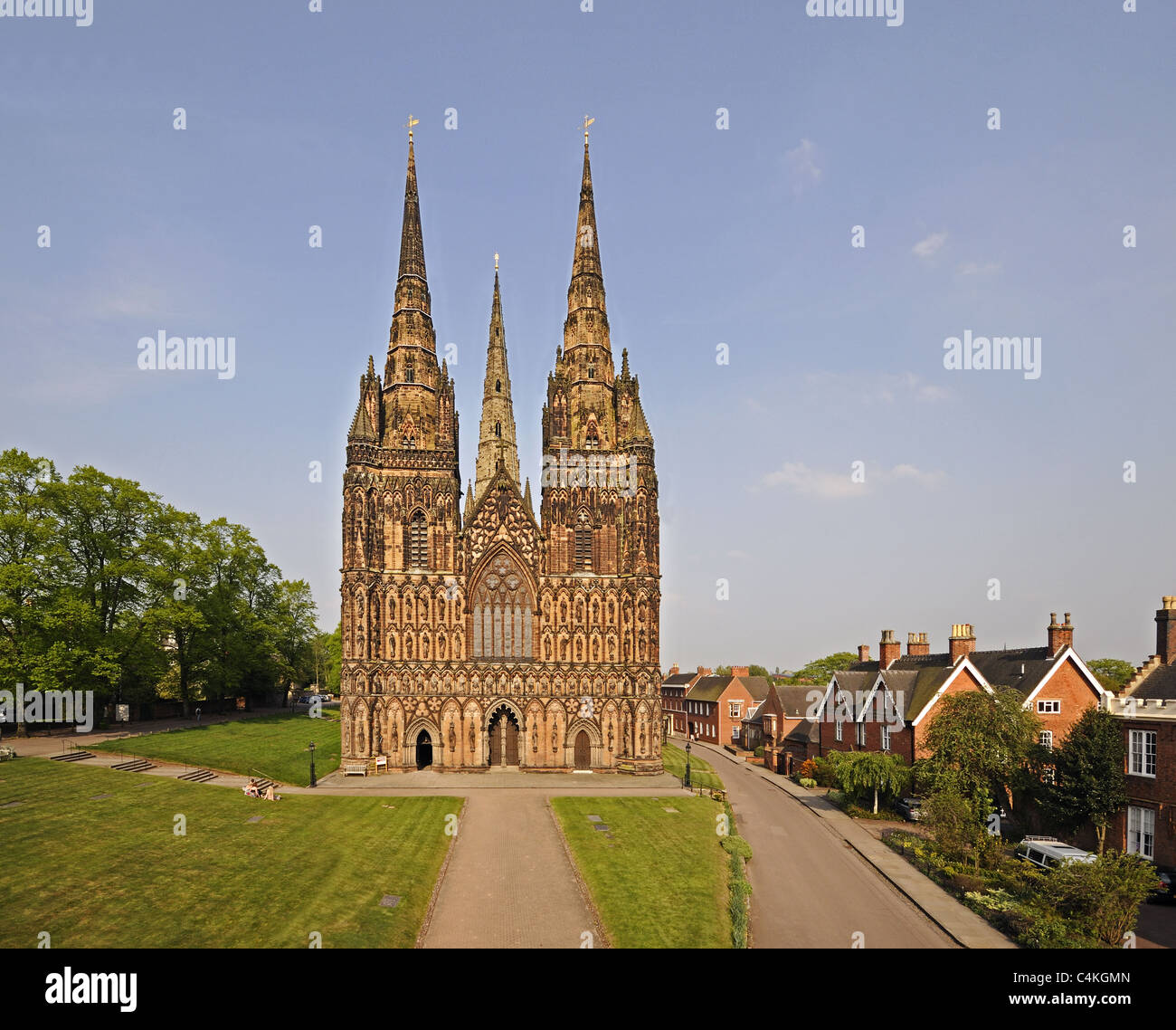 Lichfield Cathedral west front with three spires and the surrounding close and lawns with green grass and blue sky Stock Photo